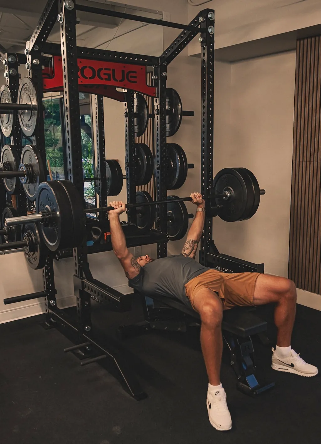 A man bench pressing a loaded barbell on a rack in a home gym.