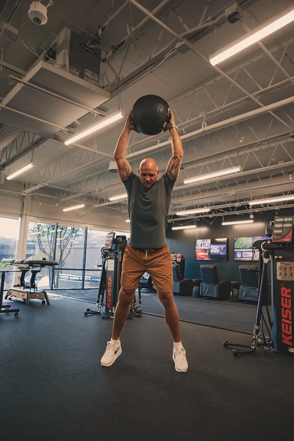 A man lifting a medicine ball overhead before a slam in a training facility.